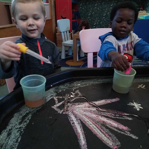 two little boys are pretending to be firefighters and putting the chalked fire out on the builders tray using pipettes