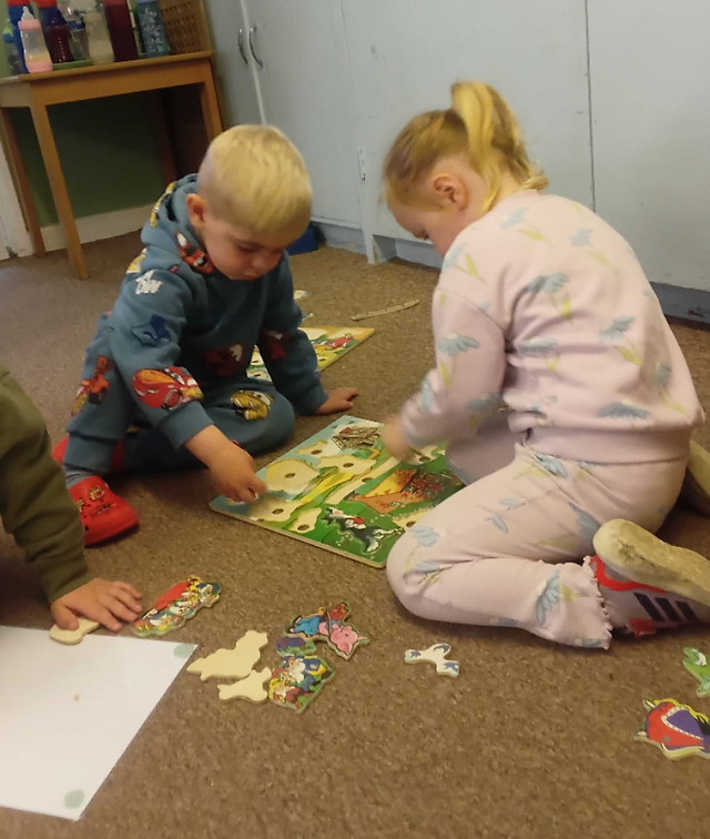 two young children sitting on a beige carpet completing a wooden inset puzzle