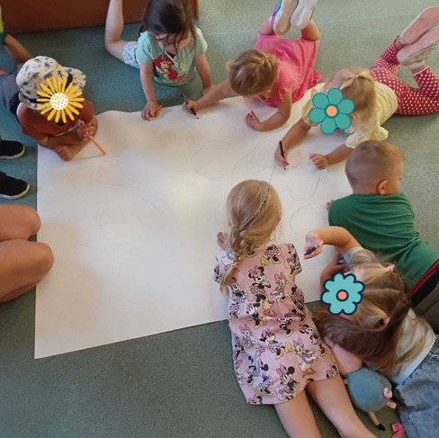 a group of small children are laying on the floor around a large piece of paper drawing with pencils