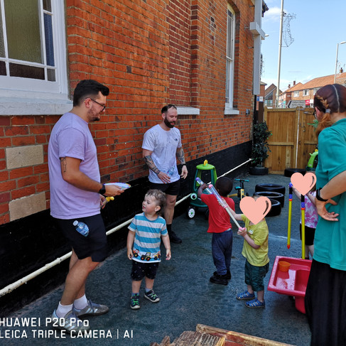 two dads and a teacher are playing waterfights with the children on a Fathers' Day Stay and Play at Fun box Day Nursery