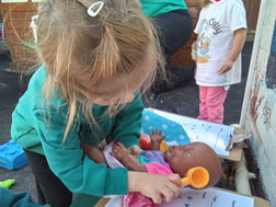 child in a Fun Box Day Nursery uniform is pretending to be a doctor examining a doll