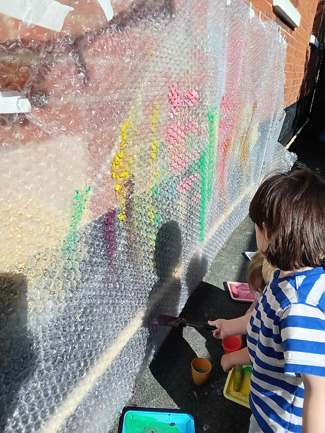 Children experiment with colourful paint on bubble wrap, discovering different marks, textures and creative possibilities through open-ended play.