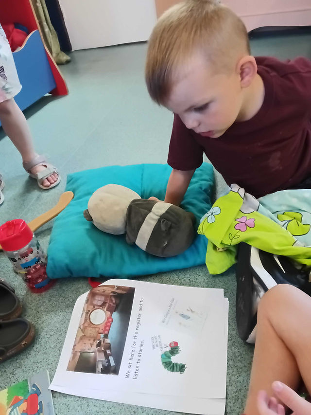 a little boy holding a toy panda is looking at some  pictures on a paper, there is a blue cushion next to him