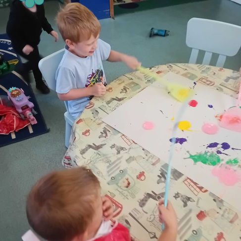 two young boys are using fly swatters to splat paint accross a big piece of paper in a nursery room