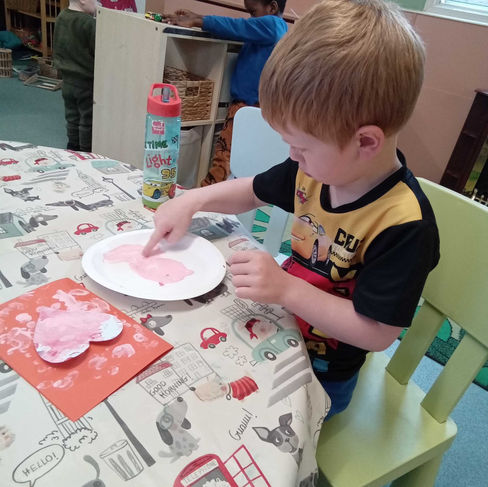 little boy is exploring paint with his fingers in a nursery setting