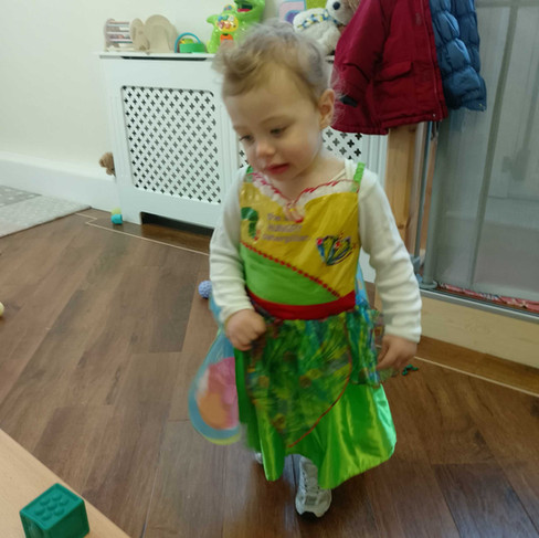 a little girl is wearing The Very Hungry Caterpillar costume and walking around, there are a few small coats hung up in the background