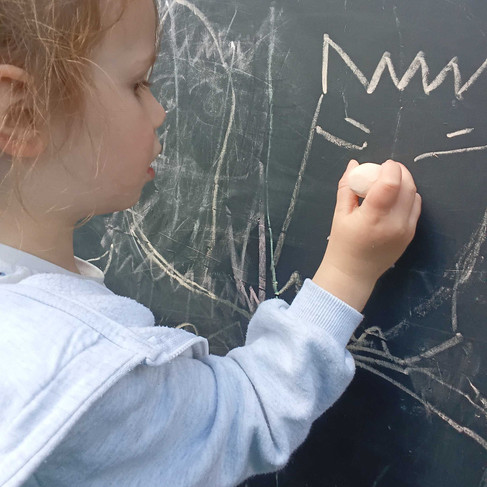 a little girl is drawing a colour monster with chalk on a blackboard in a nursery garden in Totton