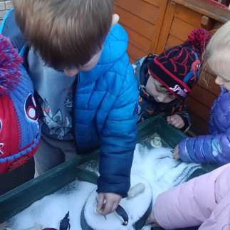 a group of young children exploring a sensory tray filled with fake snow and arctic animals
