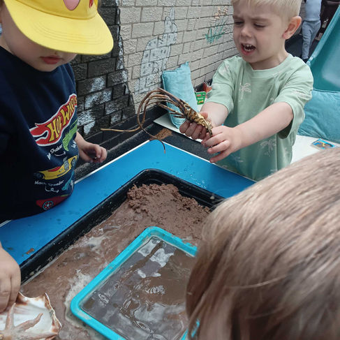 Children exploring a muddy rock pool sensory tray filled with shells and natural materials, developing observation skills, teamwork and imaginative play through hands-on learning.
