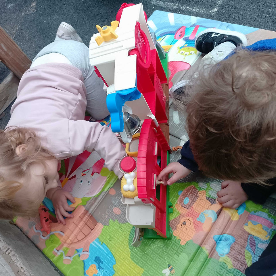 two babies are playing with a small world fire station in a nursery garden