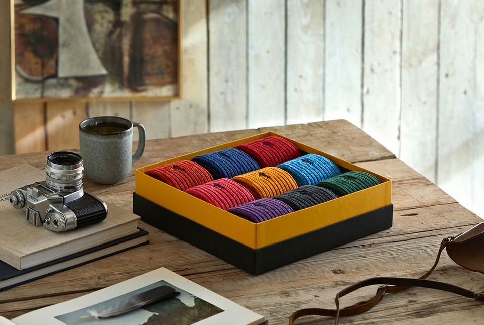 Still life photography London Sock Company box of hiking socks on a wooden background with a painting ion the background next to a cup of tea and a camera