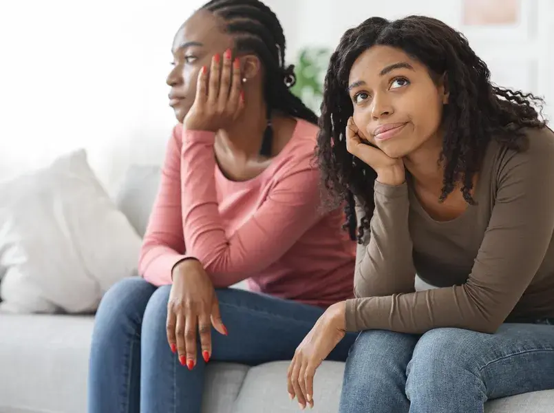 Two sad african american women sitting apart on sofa at home, had quarrel, copy space. Frustrated black ladies girlfriends feeling bad after fight, not talking, living room interior