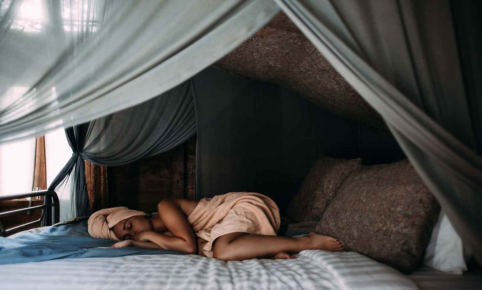 Woman lying asleep on her canopy bed with a peah colored towel on her body and her head