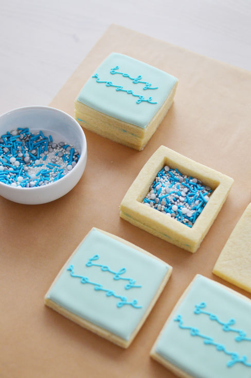 a bowl of sprinkles sits next to a baby shower cookie that says baby on it