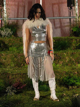 Model in silver sequinned two-piece dress with sheer draped skirt, feathered collar, and tall white boots on Sinead Gorey SS26 runway