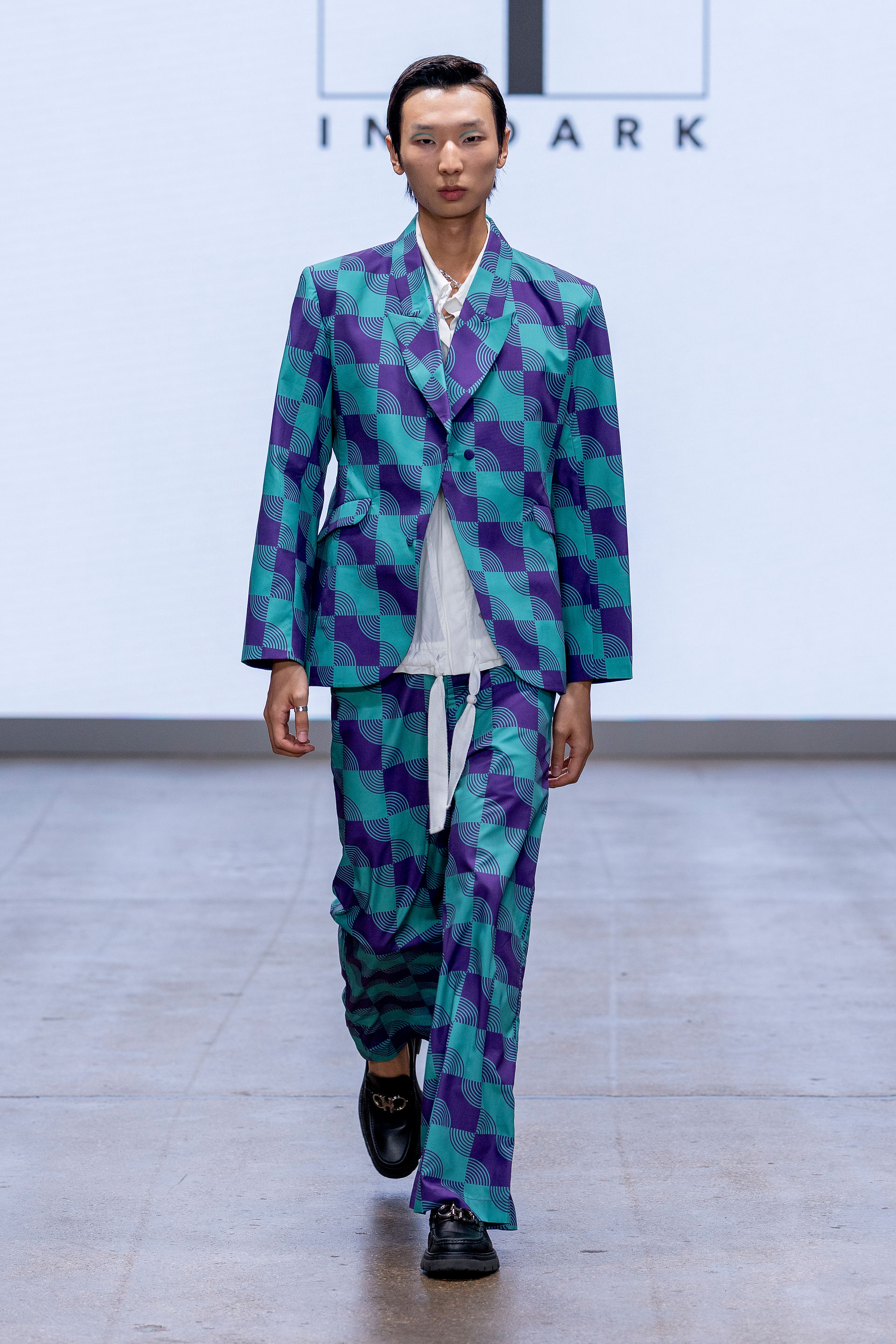 Model in a teal and purple check patterned suit over a white shirt at INF SS26