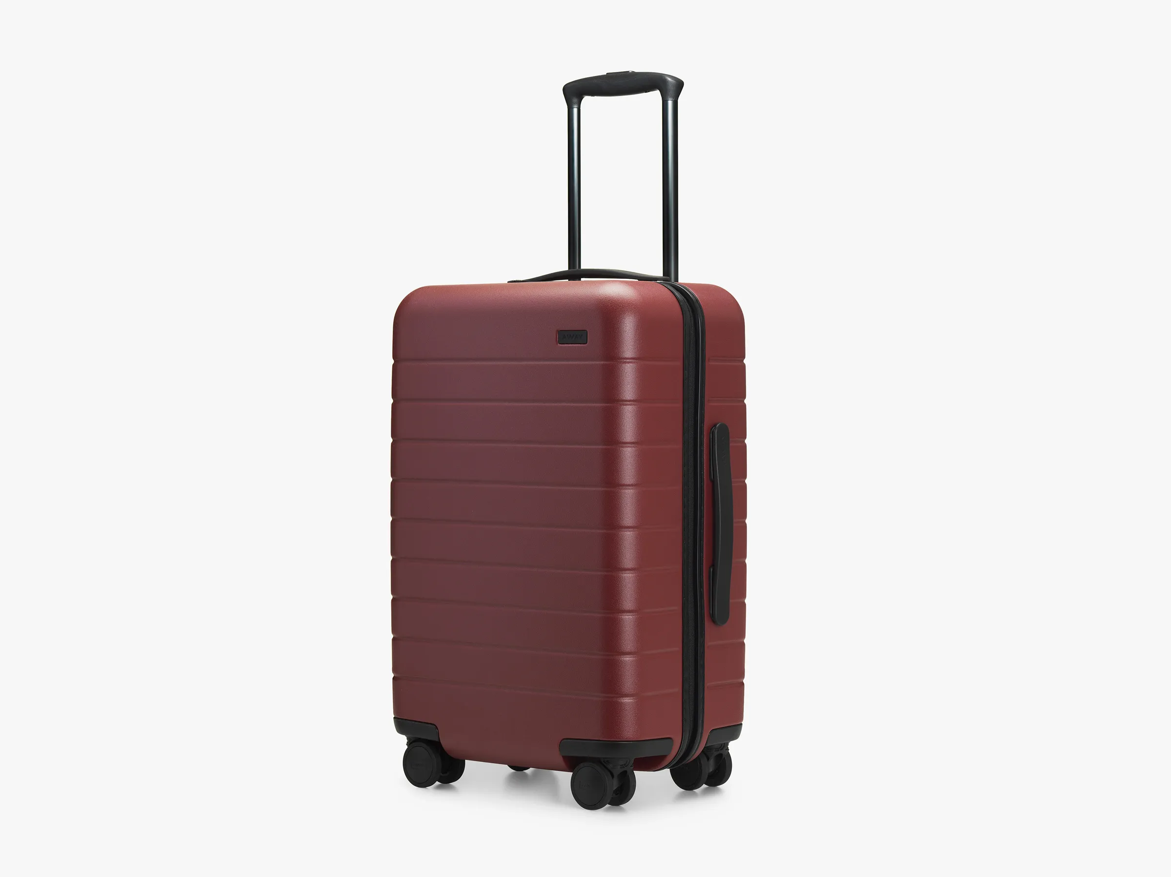 Away The Carry-On suitcase in a matte burgundy finish with black telescopic handle and four double spinner wheels, shown at a slight angle against a white background.