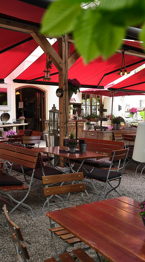 Gemütliche Gastgarten-Sitzplätze unter roter Markise