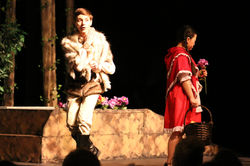 The Wolf (Noah Mims) whispers his plans for Little Red Riding Hood (Liliana Billings) to the audienc