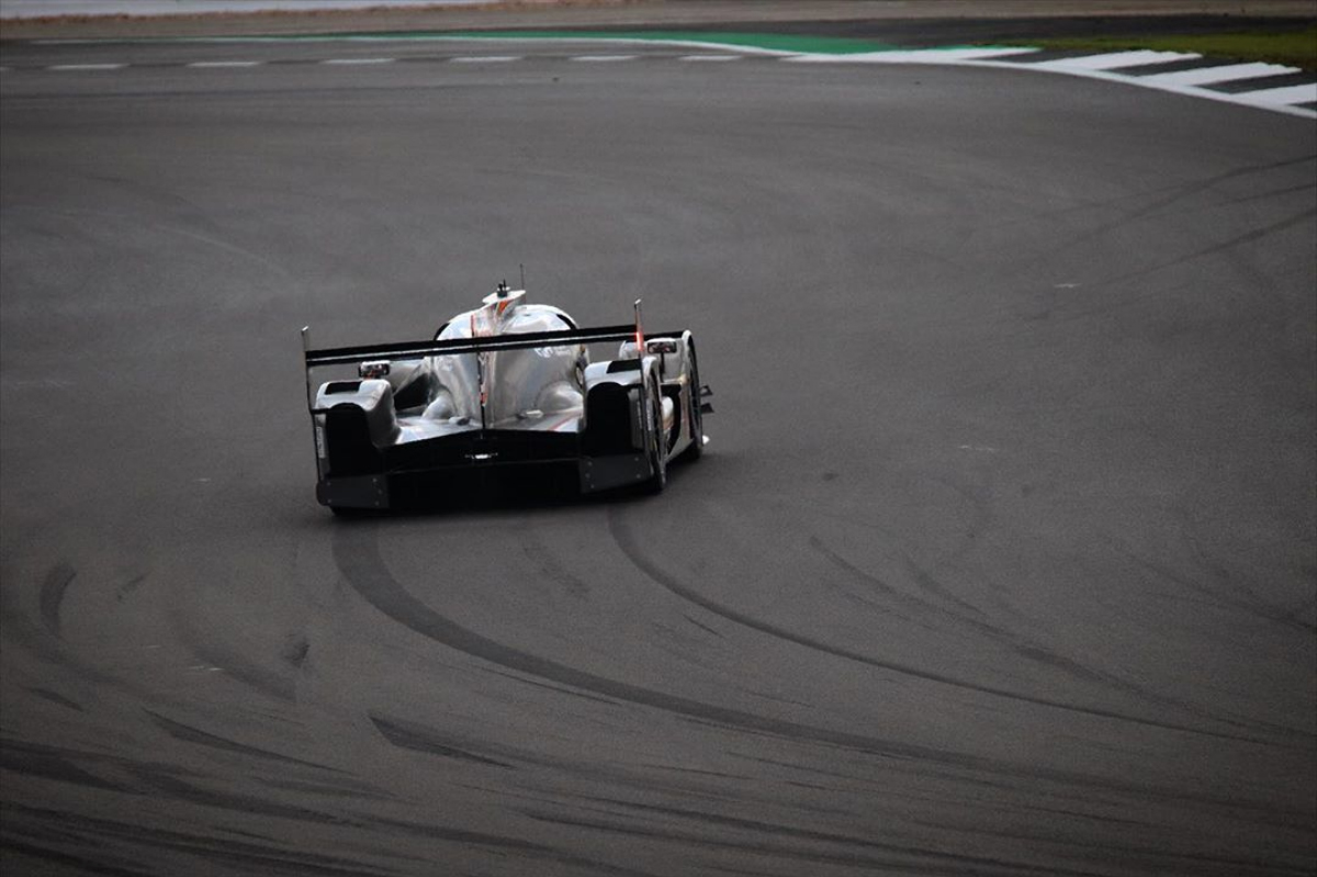 LMP racing car cornering at speed, showing body roll with tyre skid marks from lateral weight transfer visible on track