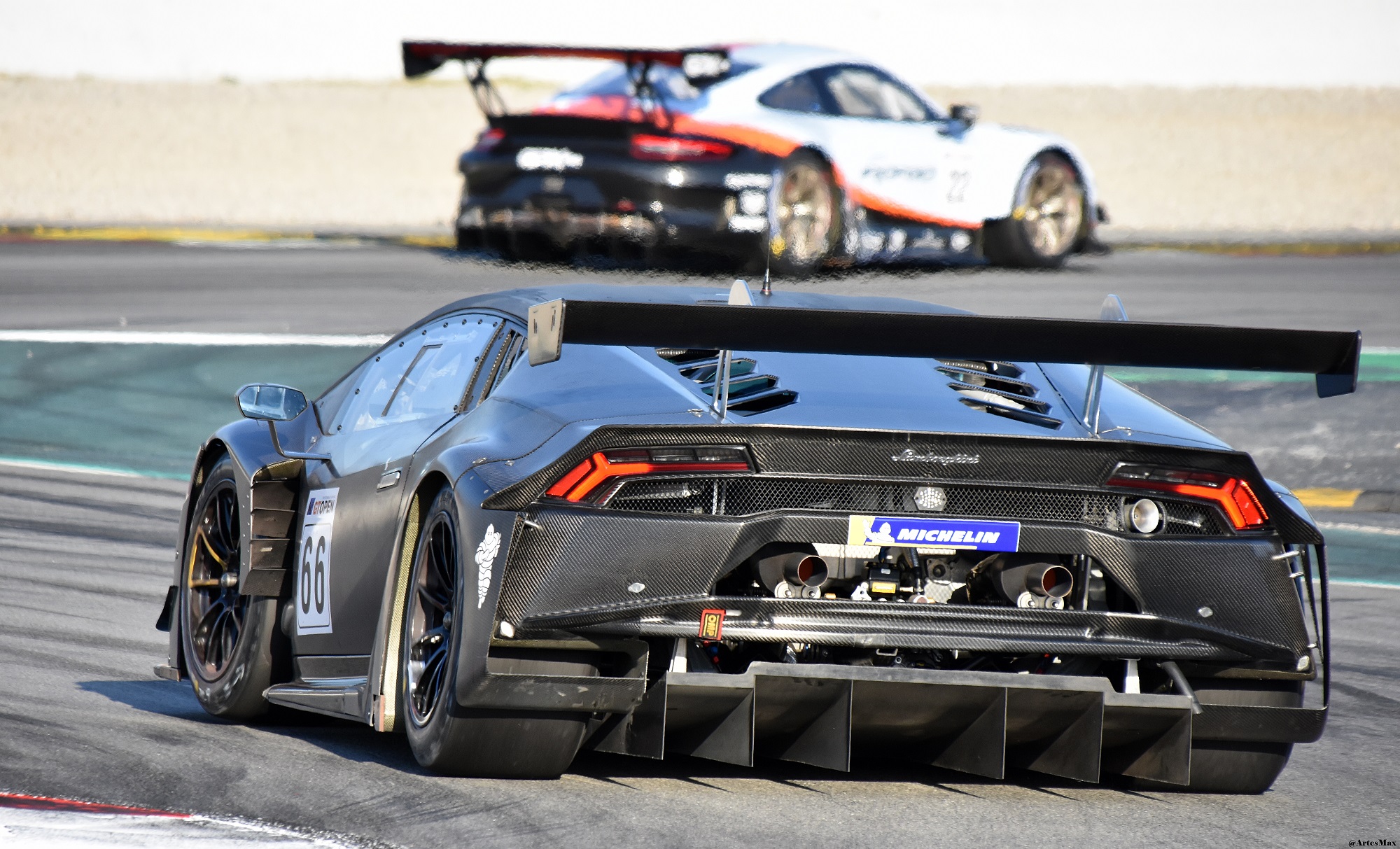 Rear view of a Lamborghini Huracán GT3 race car showing diffuser strakes and underfloor aerodynamic detailing, with a Porsche 911 GT3 in the background