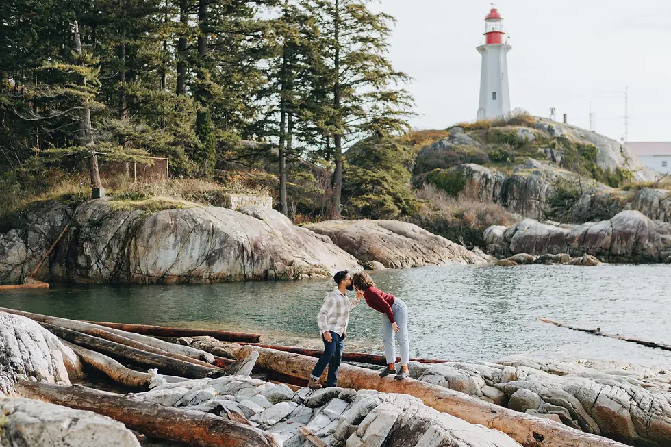 Couple standing on the rocky coastline at Lighthouse Park during a sunny November engagement session