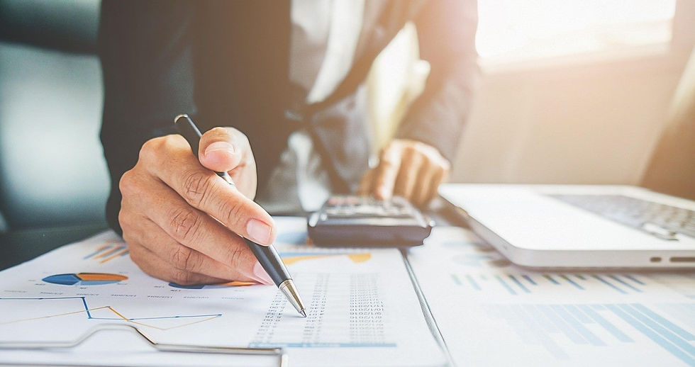 Person in a suit working at a desk with charts, using a pen and calculator.