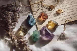 A luxurious flat lay of Virgo birthstones on a soft ivory linen background - featuring blue sapphire, carnelian, emerald, peridot, jade, and amethyst - each crystal glowing gently with earthy, calming energy. Accented with pressed herbs, dried lavender, handwritten journal pages, and delicate gold jewelry.