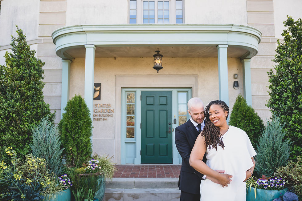 A couple smiles and embraces in front of a building with a green door, surrounded by lush greenery. Washington DC Wedding Photographers
