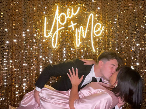 Bride and groom sharing a photo together in front of neon sign