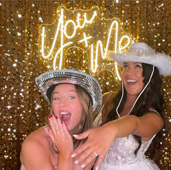 Wedding guest and bride sharing a photo together in front of golden backdrop