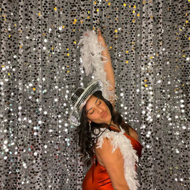 Wedding guest using white feather boas and disco hat, in front of silver sequin backdrop, at the Rabb House in Round Rock TX