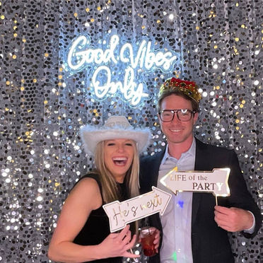 A couple in front of a silver photo booth background made of large sequins