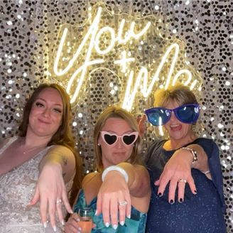 Ladies at photo booth in front of a neon sign showing off their rings for the camera