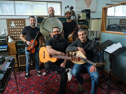 Five men posing in a music studio with various string and percussion instruments.