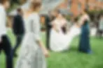 A bride laughs as friends and guests gather around her on the grass, with a brick building behind—captured perfectly by a Dorset wedding photographer.