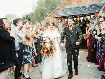 Newly married couple walking through a joyful bubble confetti exit, surrounded by smiling guests outside a rustic red brick wedding venue in Dorset.