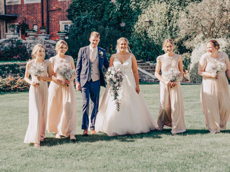 Bride and groom walking together with their bridal party, smiling and laughing in the sunshine outside a grand historic venue.