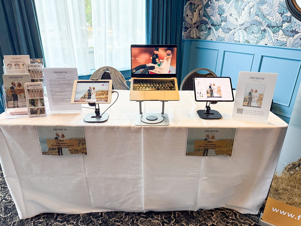 Display table for Fresh Eye Weddings at a wedding fayre, with brochures, iPads, and laptop showing photography and videography work.