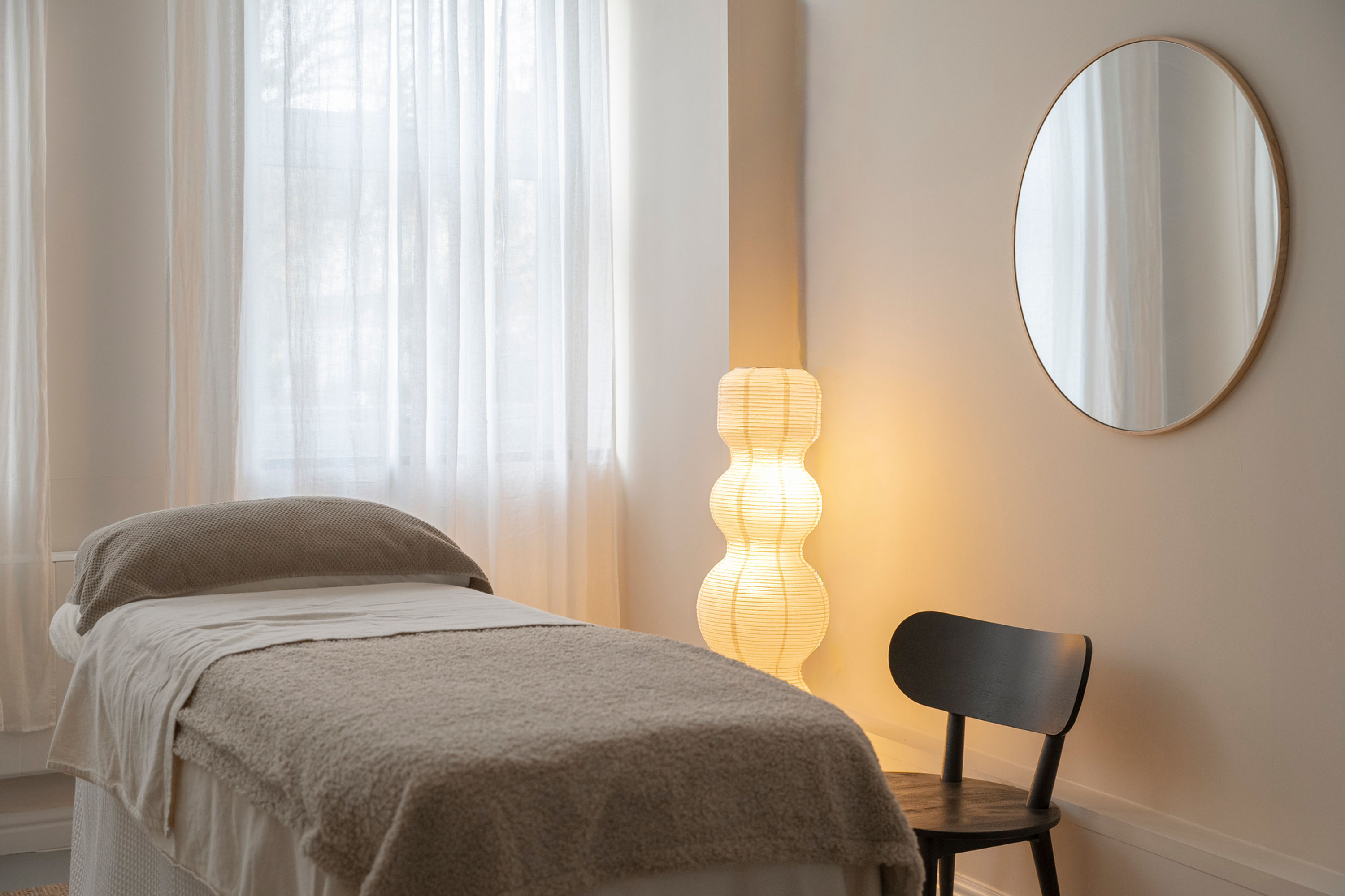 A photo of Studio Lomas. There is a massage table, soft lighting and a chair