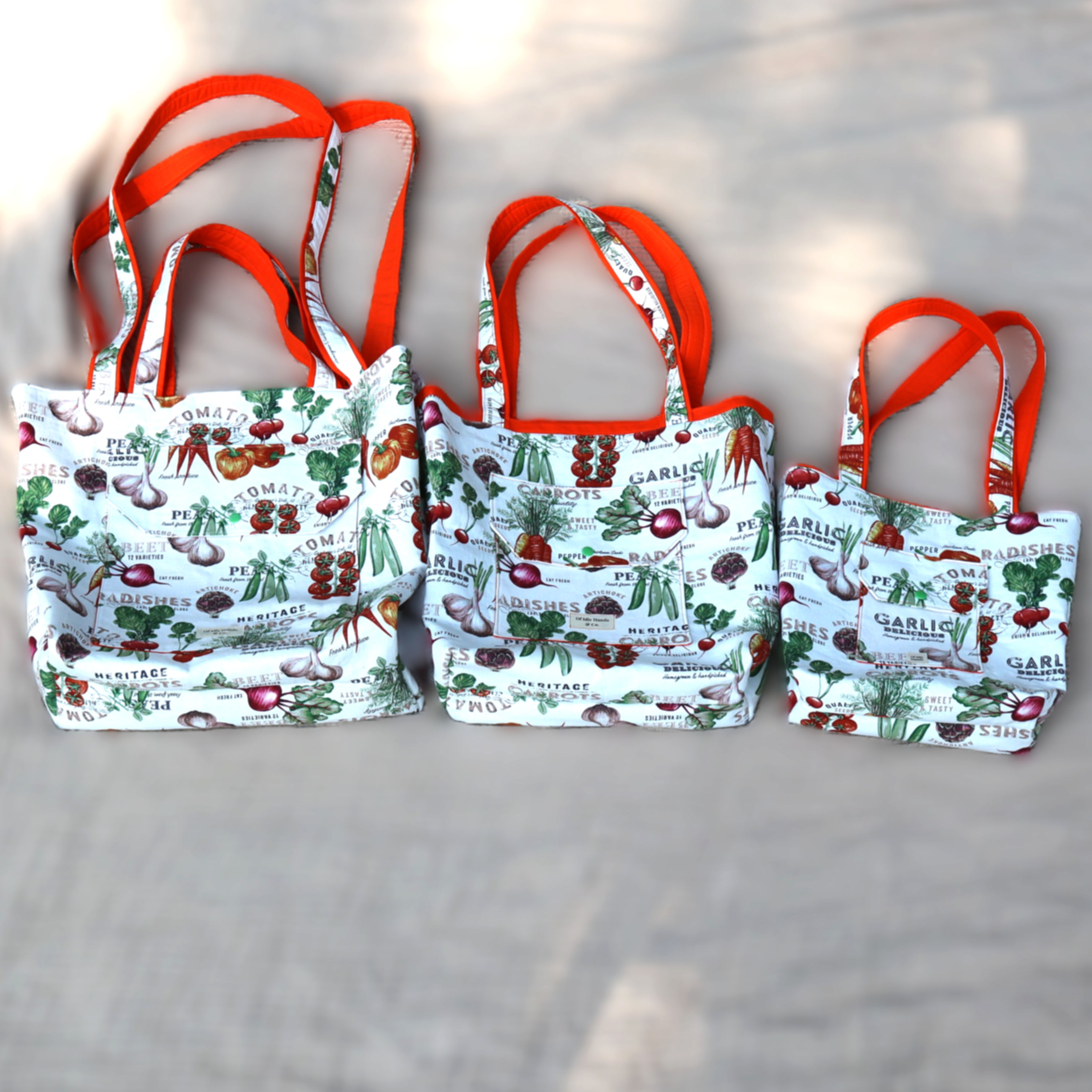Three sizes of vegetable print market tote bags with orange straps
