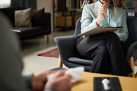 Woman in light blue jacket, black pants sitting in office chair taking notes during a therapy session