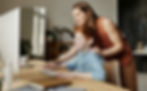 Boy with ginger hair looking at computer with foster parent looking over shoulder helping
