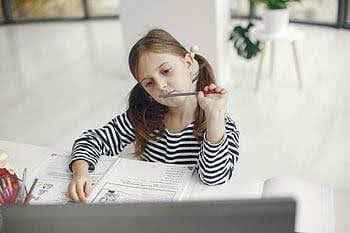 girl sitting at desk with her pencil by her mouth in deep thought.