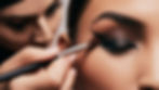 Close-up of a hand blending eyeliner with a smudge brush on a model's eye. The focus is on the brush movement, with the eyeliner gradually softening into a smoky finish.