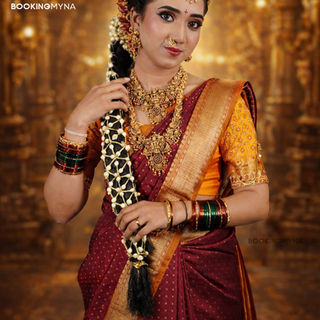 South Indian bride in maroon and gold silk saree with traditional bridal jewellery and jasmine braid, showcasing professional bridal makeup and hairstyling services by BookingMyna certified makeup artists.