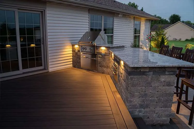 A backyard patio with a built-in grill space at night designed and installed by Knob Hill Landscape Company of Springfield, Illinois. 