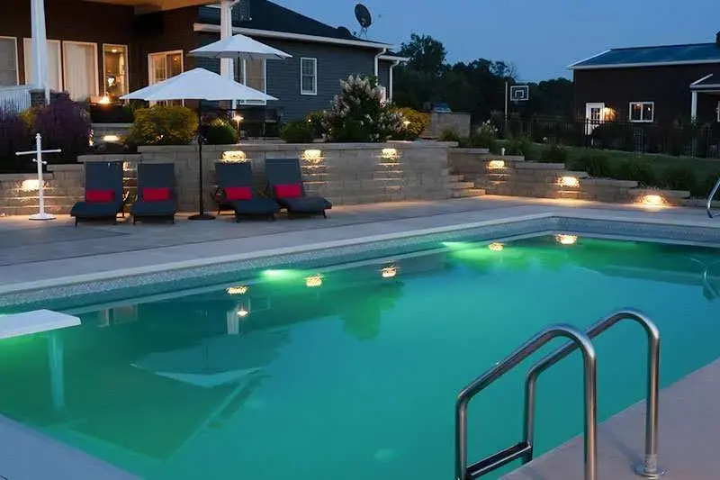 A large in ground pool at night with a large patio on the back of the modern residential home. Space designed by Knob Hill Landscape Company of Springfield, Illinois.
