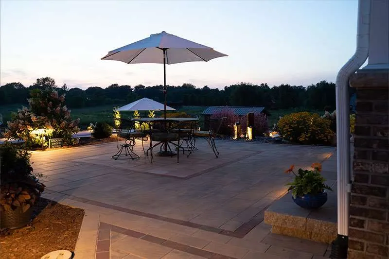 A large patio space for a modern residential home with seating, concrete patio pavers, and flowering plants designed by Knob Hill Landscape Company in Springfield, Illinois.