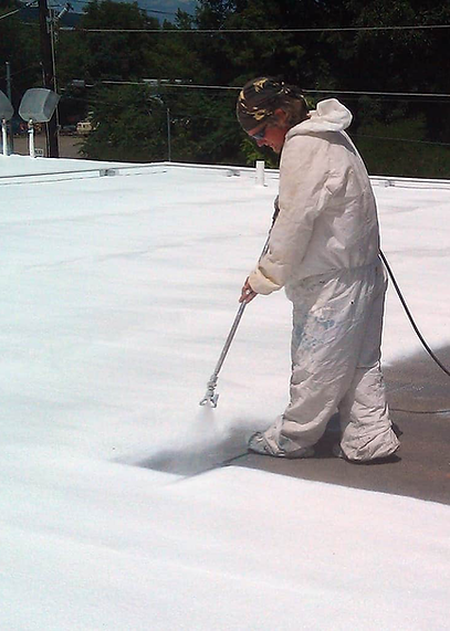Employee of I-57 Roofing of Illinois dressed all in white, spraying white protective coating onto a commercial rooftop.